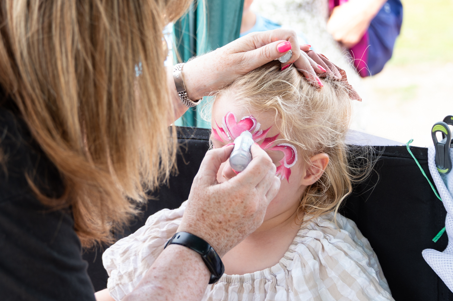 A lady painting a child's face in pink