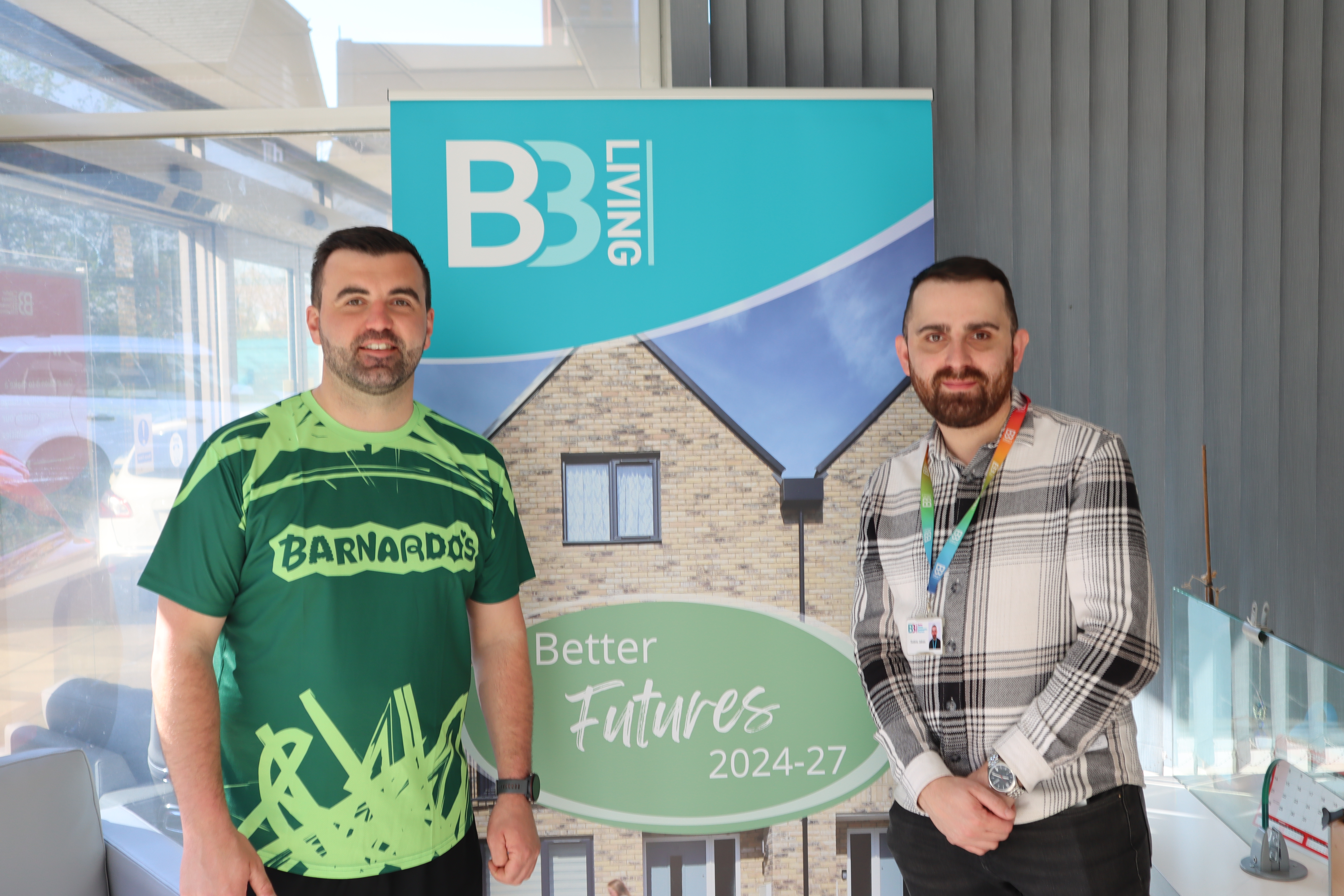 Two men smiling standing in front of a B3Living banner. The banner reads 'Better Futures 2024-27'