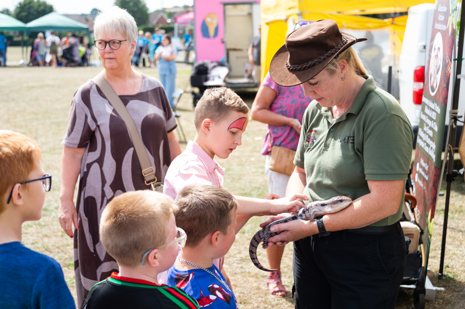 Child petting a reptile held by a woman while three other kids look