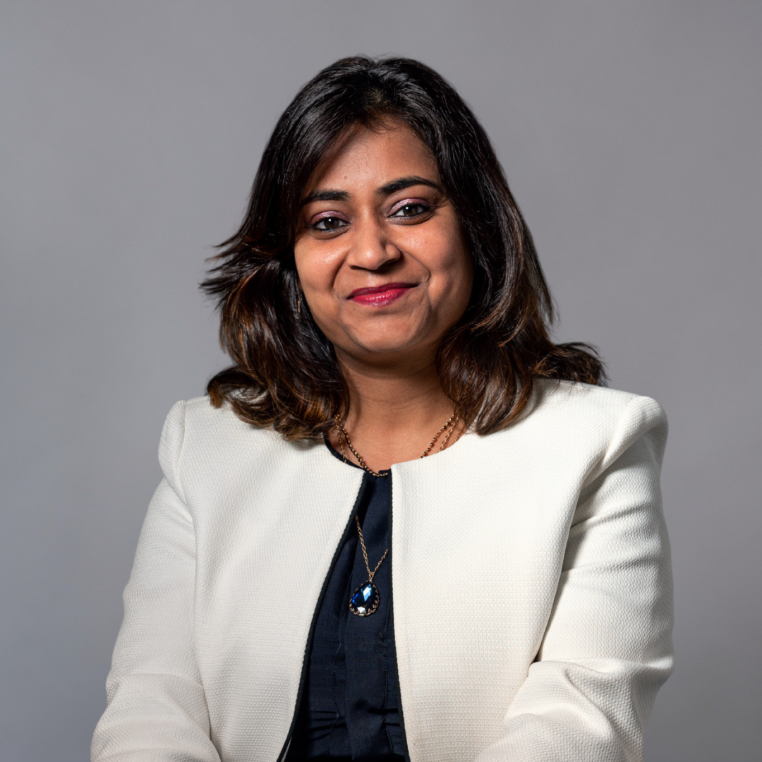 A woman smiling. She has shoulder-length hair and is wearing a white blazer