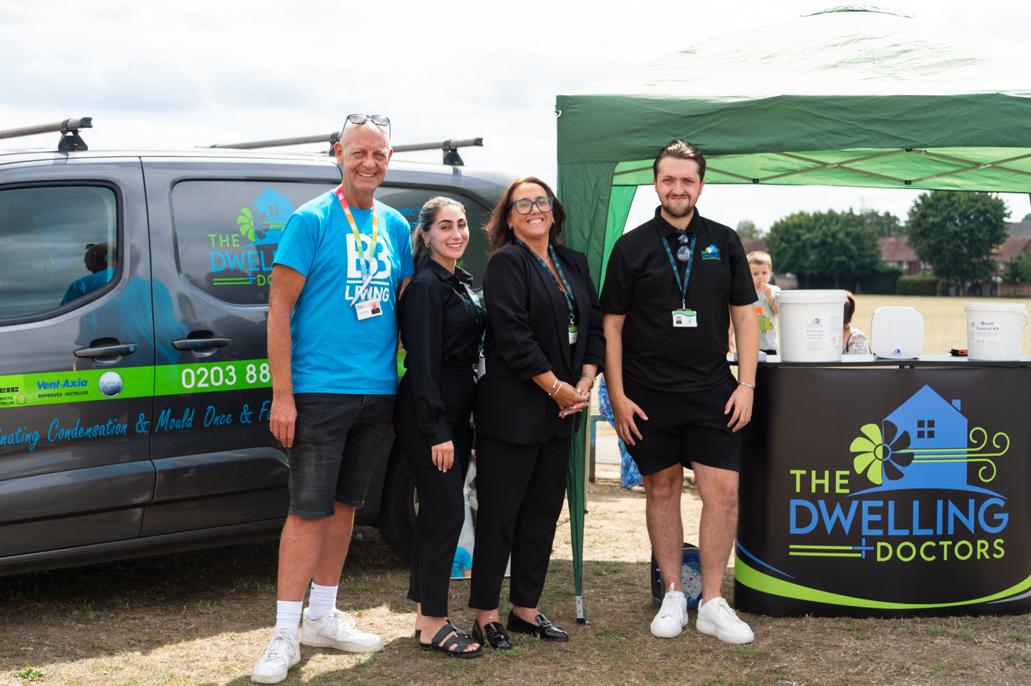 Two smiling men and two women standing in front of a van and a stall that says Dwelling Doctors